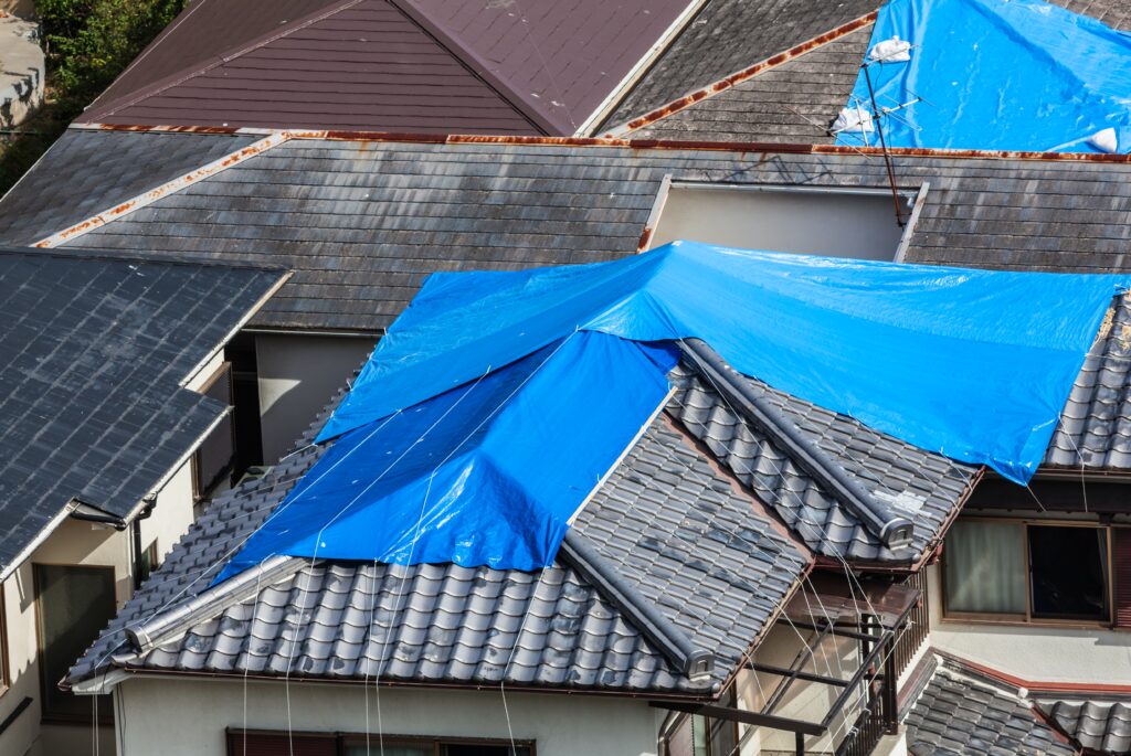 Houses with Damaged Tiled Roof Covered with Blue Tarp.